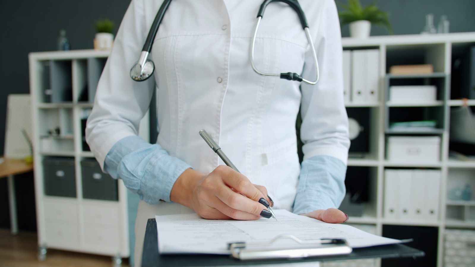 Medica con bata blanca escribiendo en el expediente clinico de un paciente sobre una tabla portapapeles