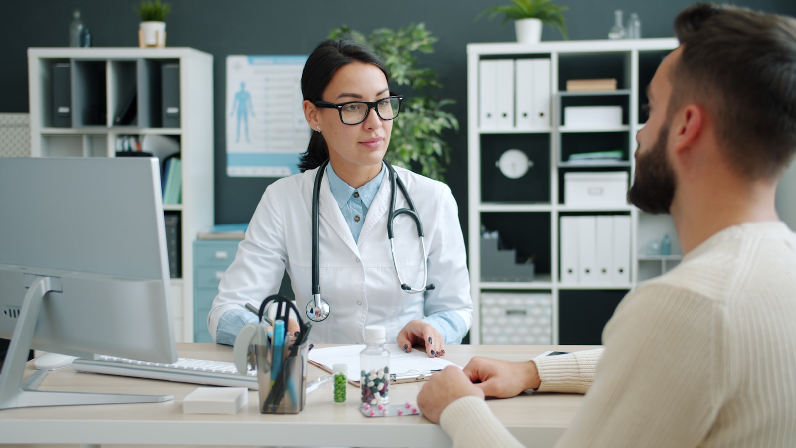 Medica especialista con bata blanca y estetoscopio atendiendo a un paciente en su consultorio